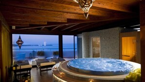 Un jacuzzi en una habitación con vistas al mar, vigas de madera en el techo y una pared de piedra.
