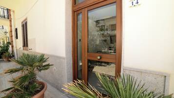 L’entrée d’un hôtel, avec une porte en bois, un pot de fleurs et un panneau indiquant le numéro de l’hôtel sur le mur.