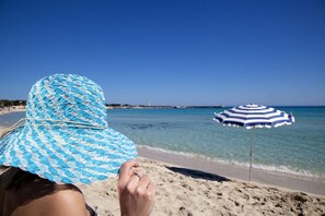 A beach scene with a person sitting under a striped beach umbrella, overlooking the sea. - Miraspiaggia (San Vito Lo Capo)