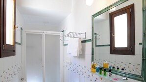 Une salle de bain avec un lavabo blanc, deux toilettes, une douche et un miroir avec éclairage intégré.
