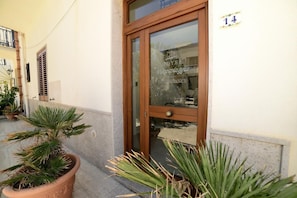 A hotel entrance with a wooden door, a potted plant, and a number sign. - Miraspiaggia (San Vito Lo Capo)