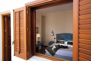 Habitació d'hotel amb una porta corredissa de fusta, un llit amb almoinades estampades, una taula de nit amb una làmpada i una lluminària penjada a la paret.