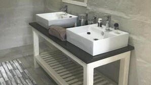A bathroom with two white sinks, a mirror above them, and a wooden bench below. - Visgraat Luxury Self Catering Unit (uMhlabuyalingana)
