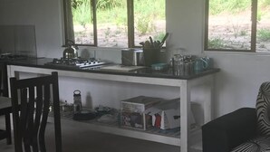 A compact kitchen with a gas stove, a kettle, and various kitchen utensils on the countertop. There is a chair and a sofa in the room. - Visgraat Luxury Self Catering Unit (uMhlabuyalingana)