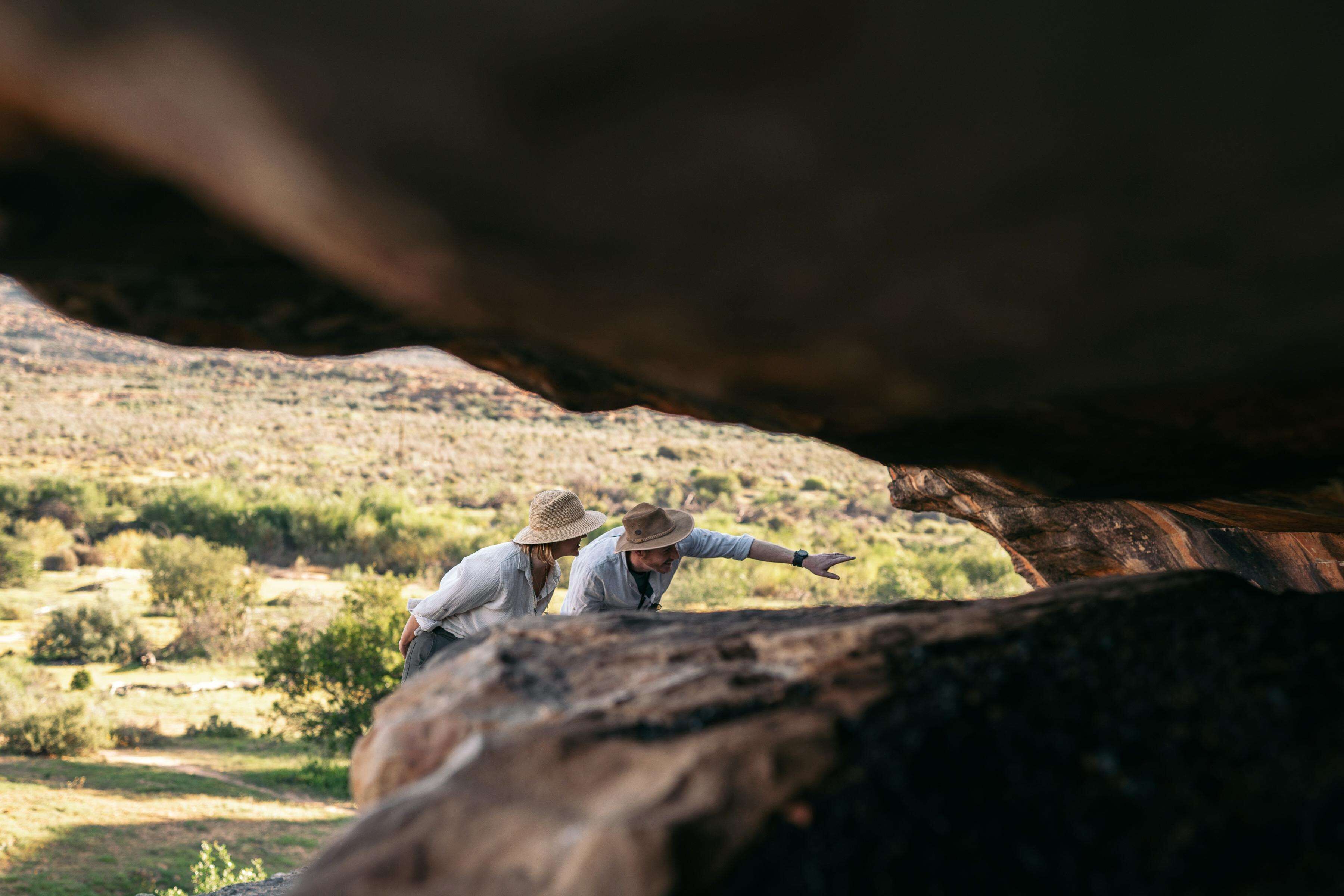 Two people standing on a rock with a natural landscape in the background.
