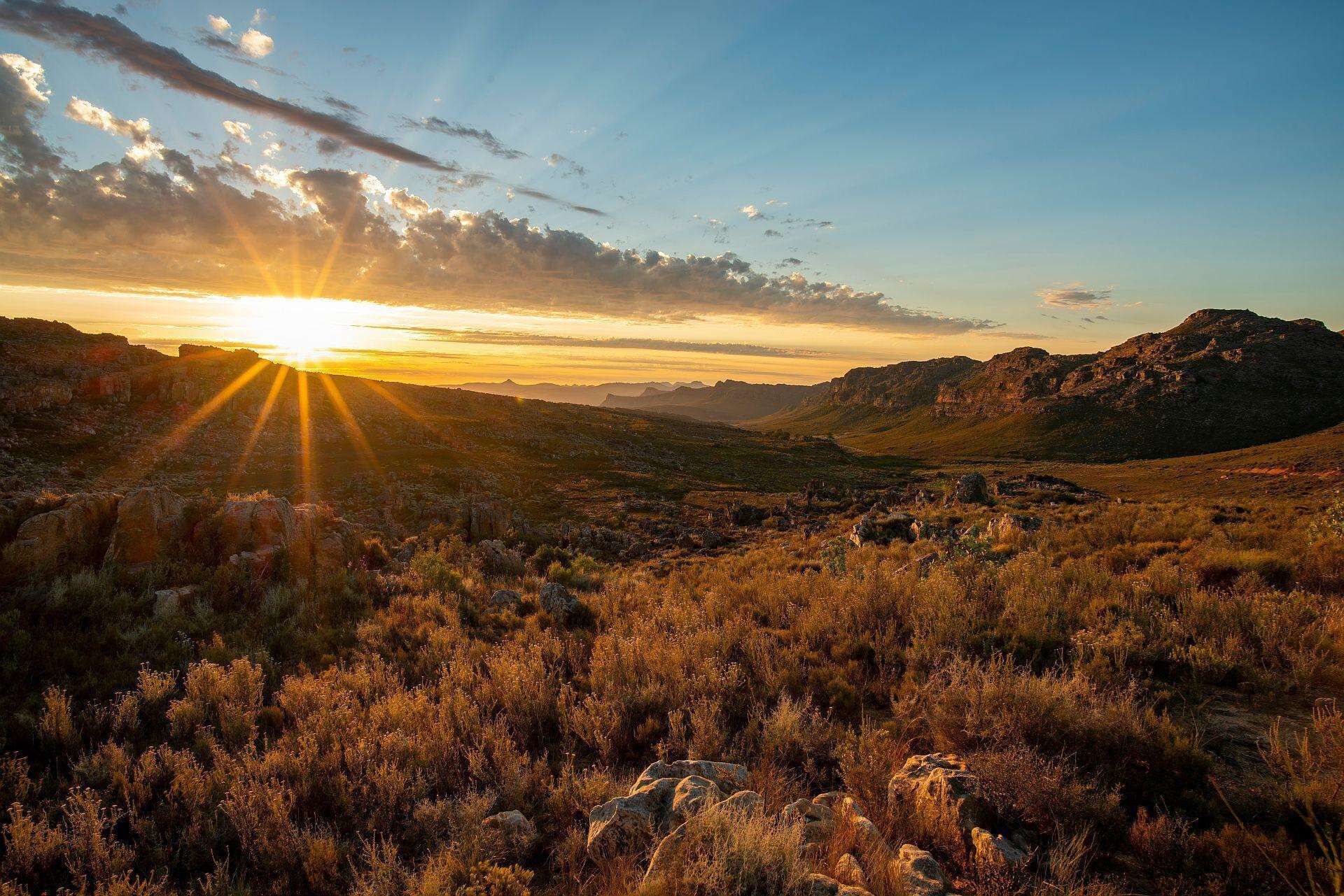 Eine Landschaft bei Sonnenuntergang, felsiges Gelände und spärliche Vegetation.