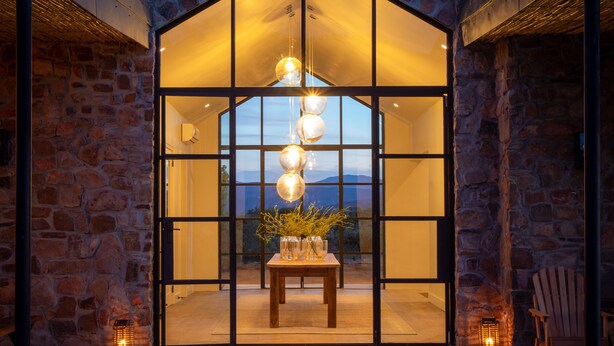 A modern house with a stone facade, large glass windows, and a wooden table with a vase of flowers in the center. - Simbavati Cederberg Ridge (Cederberg)