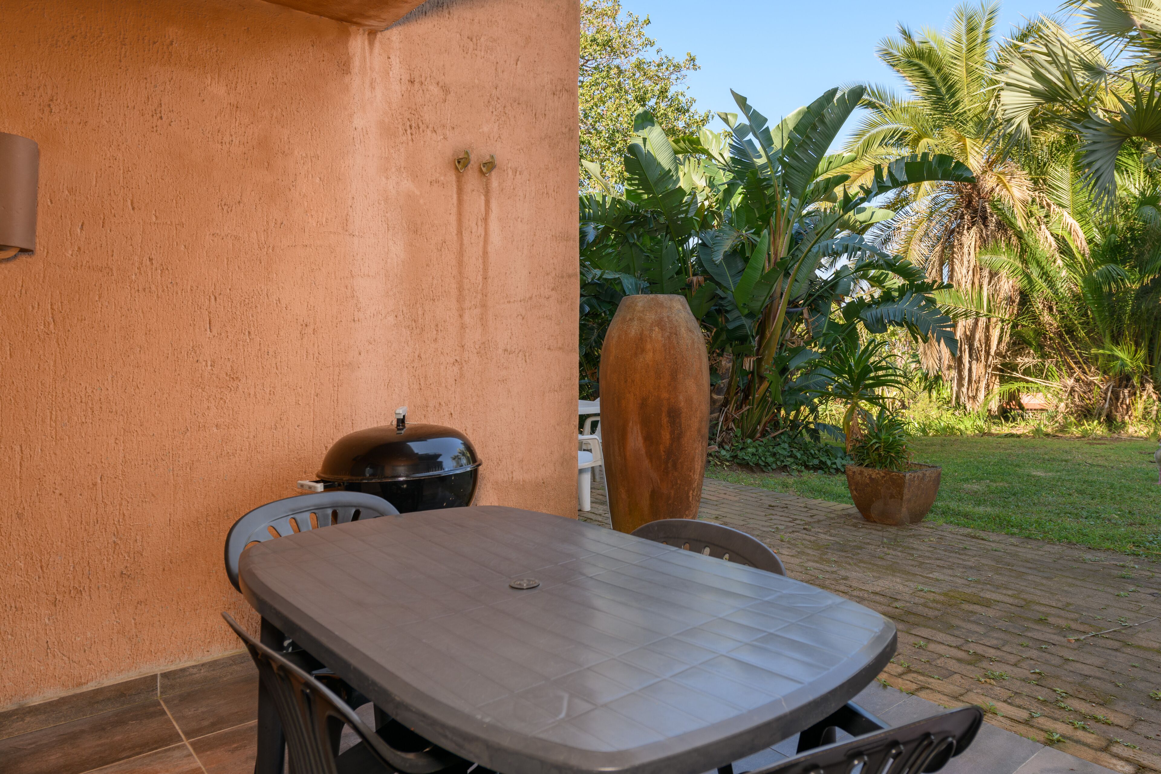 An outdoor patio with a table and chairs, a barbecue grill, and a large planter.