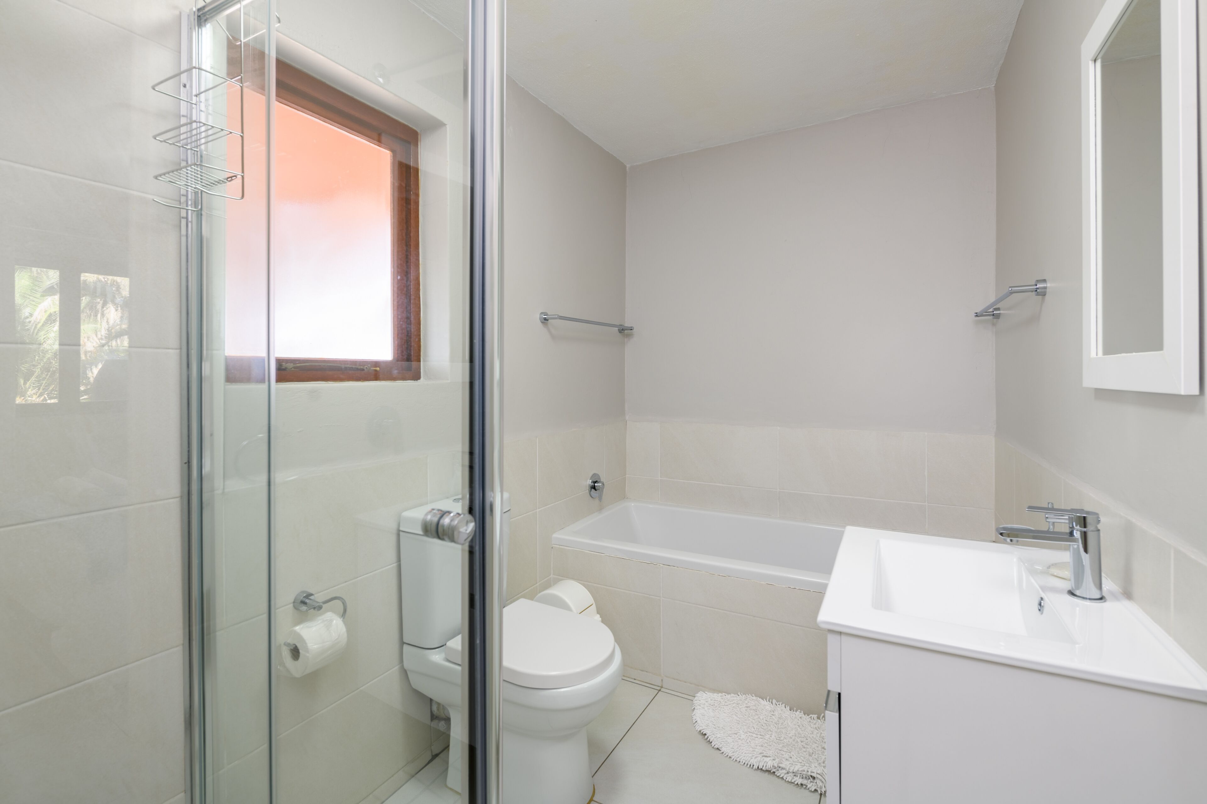 A modern bathroom with a glass shower enclosure, a toilet, a bathtub, and a sink.