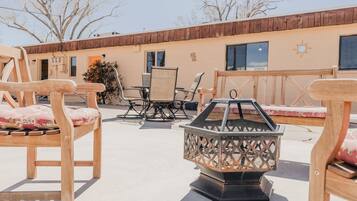 An outdoor patio area with wooden furniture, a metal fire pit, and a building with a wooden facade in the background.