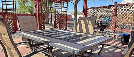Une terrasse extérieure avec une table et des chaises, un barbecue et une pergola.
