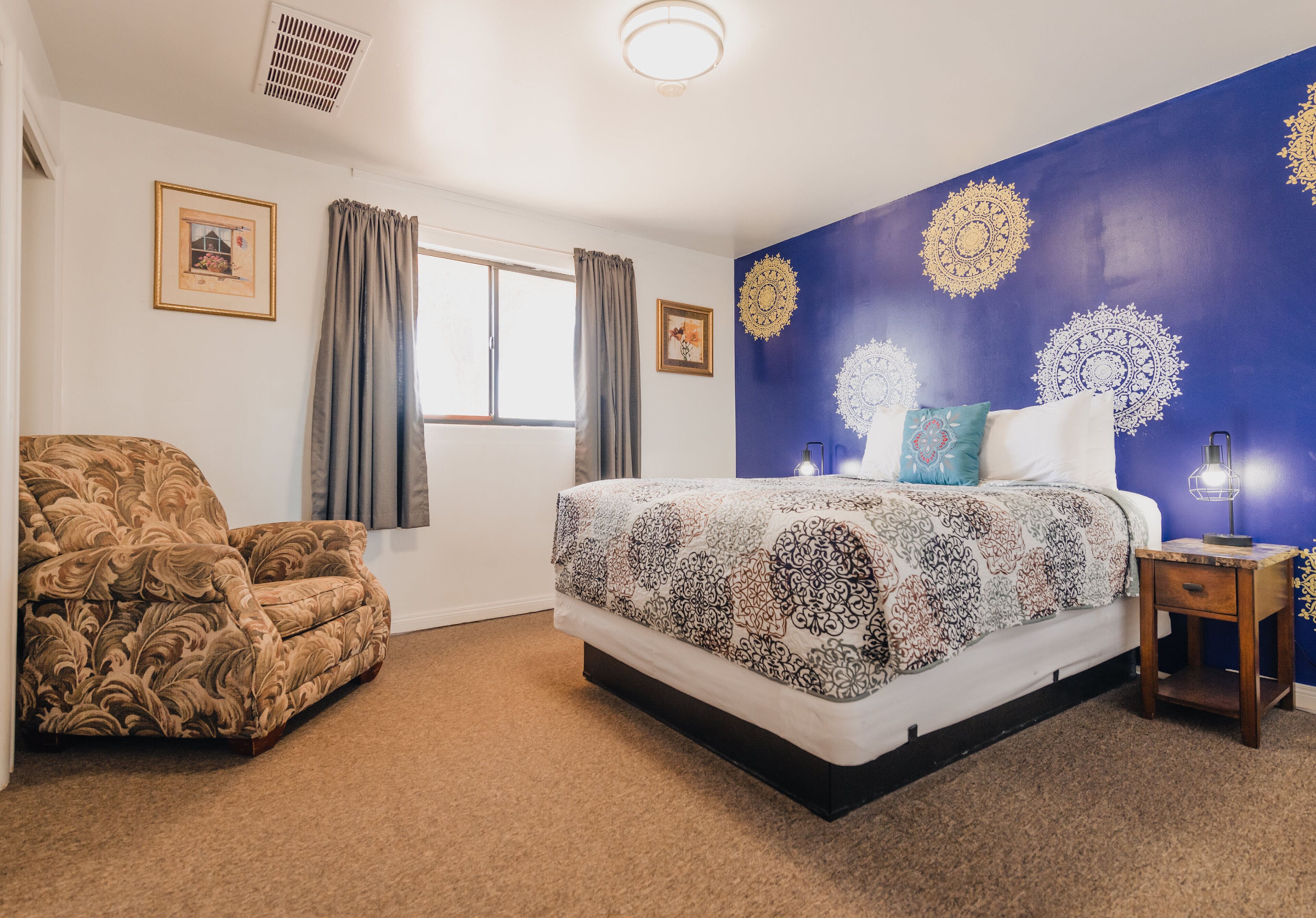 A bedroom with a bed, a chair, a nightstand, and decorative wall art.