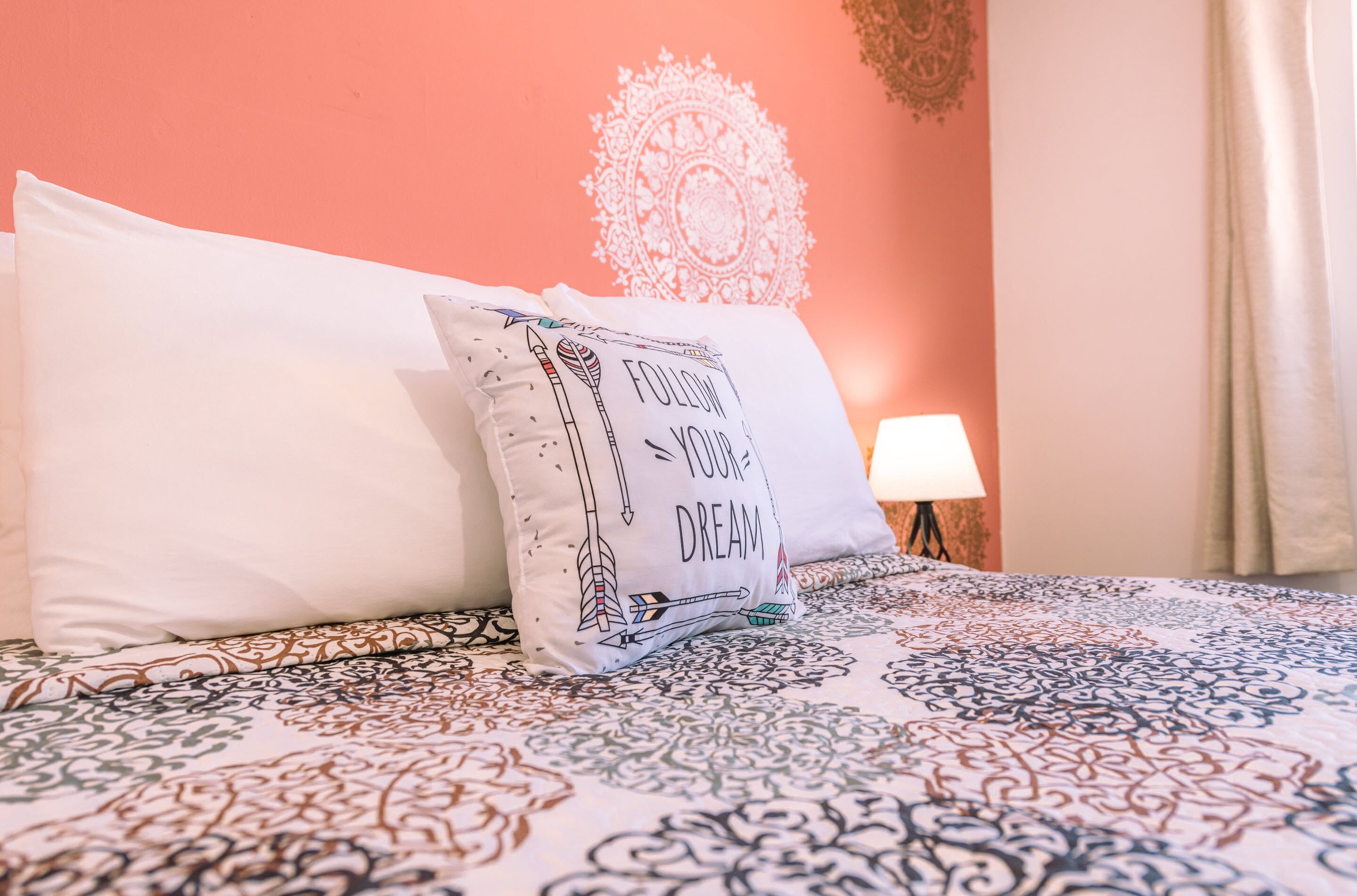 A neatly made bed with patterned bedding and a pillow with a motivational quote.