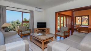A spacious living room with a flat-screen TV, comfortable seating, and large windows offering a view of the outdoors. - San Lameer Villa Rentals 3704 (Southbroom)