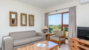A living room with a sofa, a coffee table, a TV stand, and a chair. There are three wall mirrors and a window with curtains. - San Lameer Villa Rentals 3704 (Southbroom)