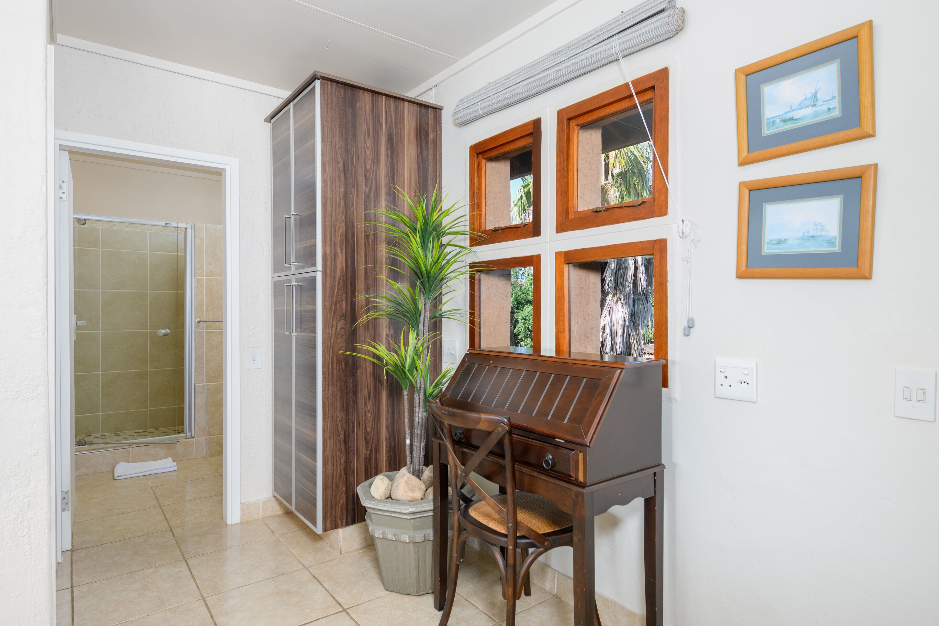 A bathroom with a shower, a wooden cabinet, a potted plant, and framed pictures on the wall.