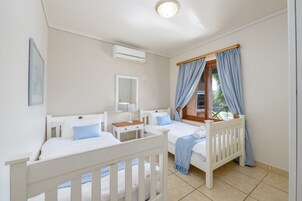 Un dormitorio con dos camas, una ventana con cortinas, una mesita de noche y un aire acondicionado de pared.