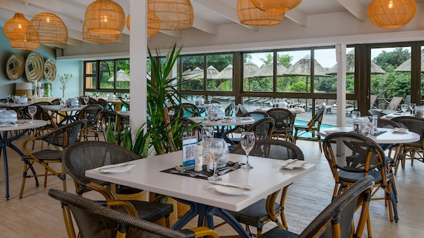 Un restaurante con sillas de mimbre, mesas blancas y lámparas colgantes de mimbre.