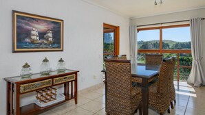 Un comedor con sillas de mimbre, una mesa de madera y una consola con cubierta de vidrio y objetos decorativos.