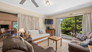 Ein geräumiges Wohnzimmer mit einer Couch, zwei Sesseln, einem Couchtisch, einem Fernseher und einem Kamin.