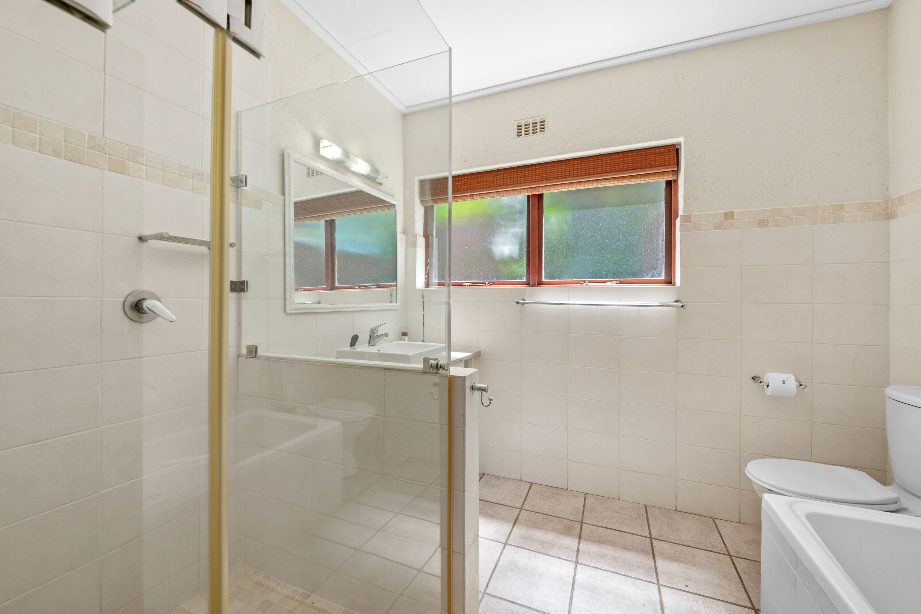 Un baño moderno con cabina de ducha de vidrio, un lavamanos, un inodoro y una ventana con persianas.
