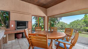 Eine überdachte Terrasse mit einem runden Holztisch und Stühlen, einem eingebauten Grill und einem Fernseher.