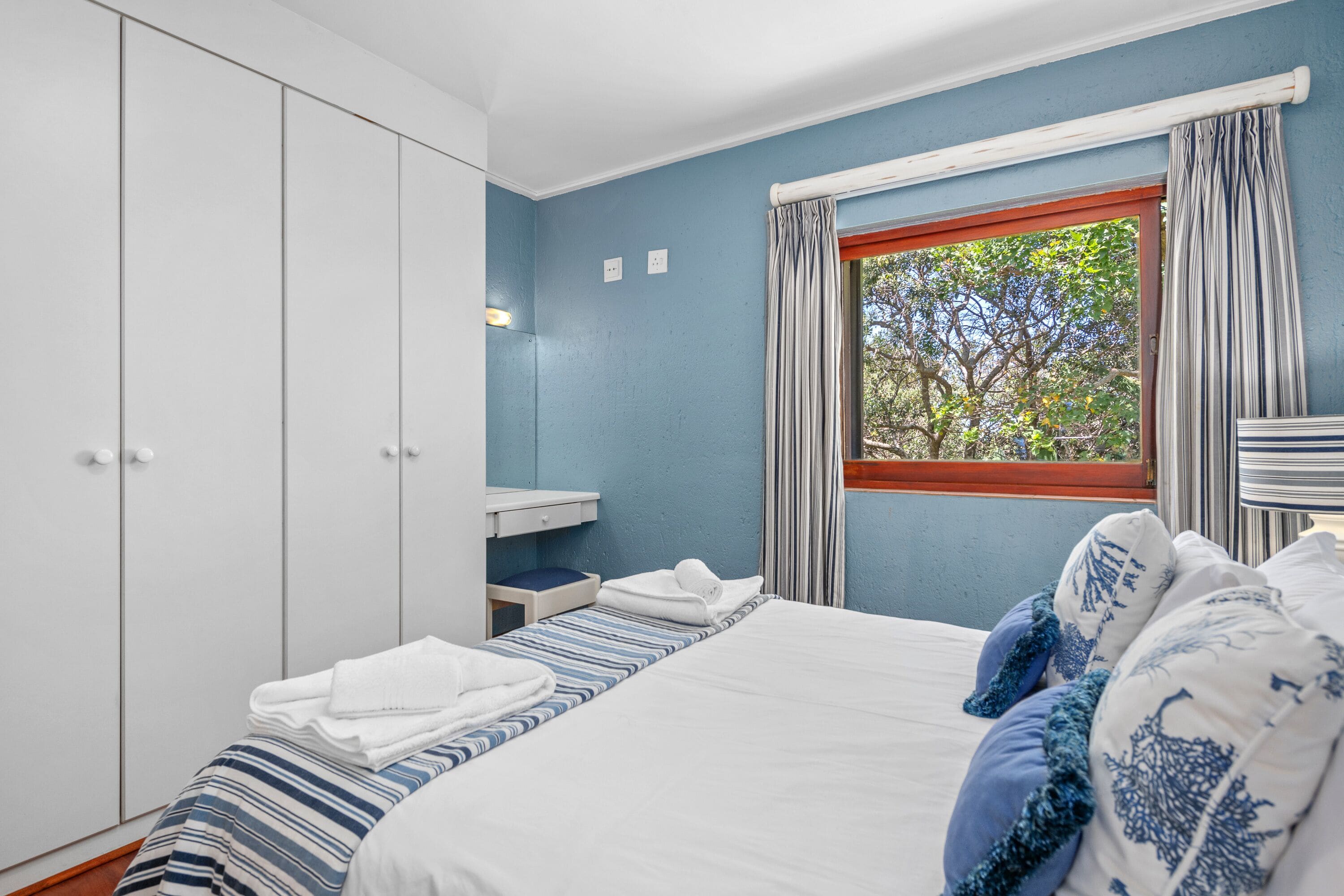 A bedroom with a bed, a wardrobe, a window with curtains, and a view of trees.