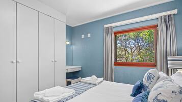 A bedroom with a bed, a wardrobe, a window with curtains, and a view of trees.