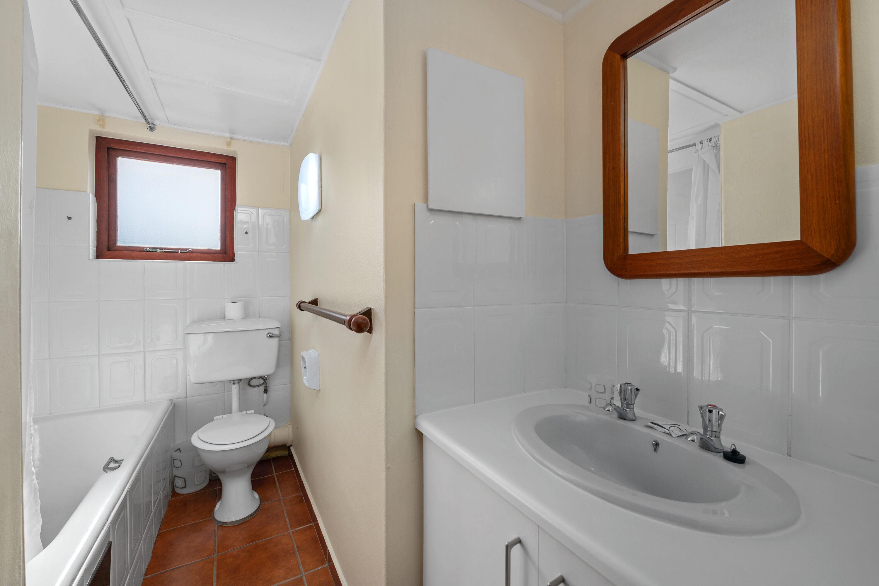 Et badeværelse med toilet, vask, badekar og spejl.