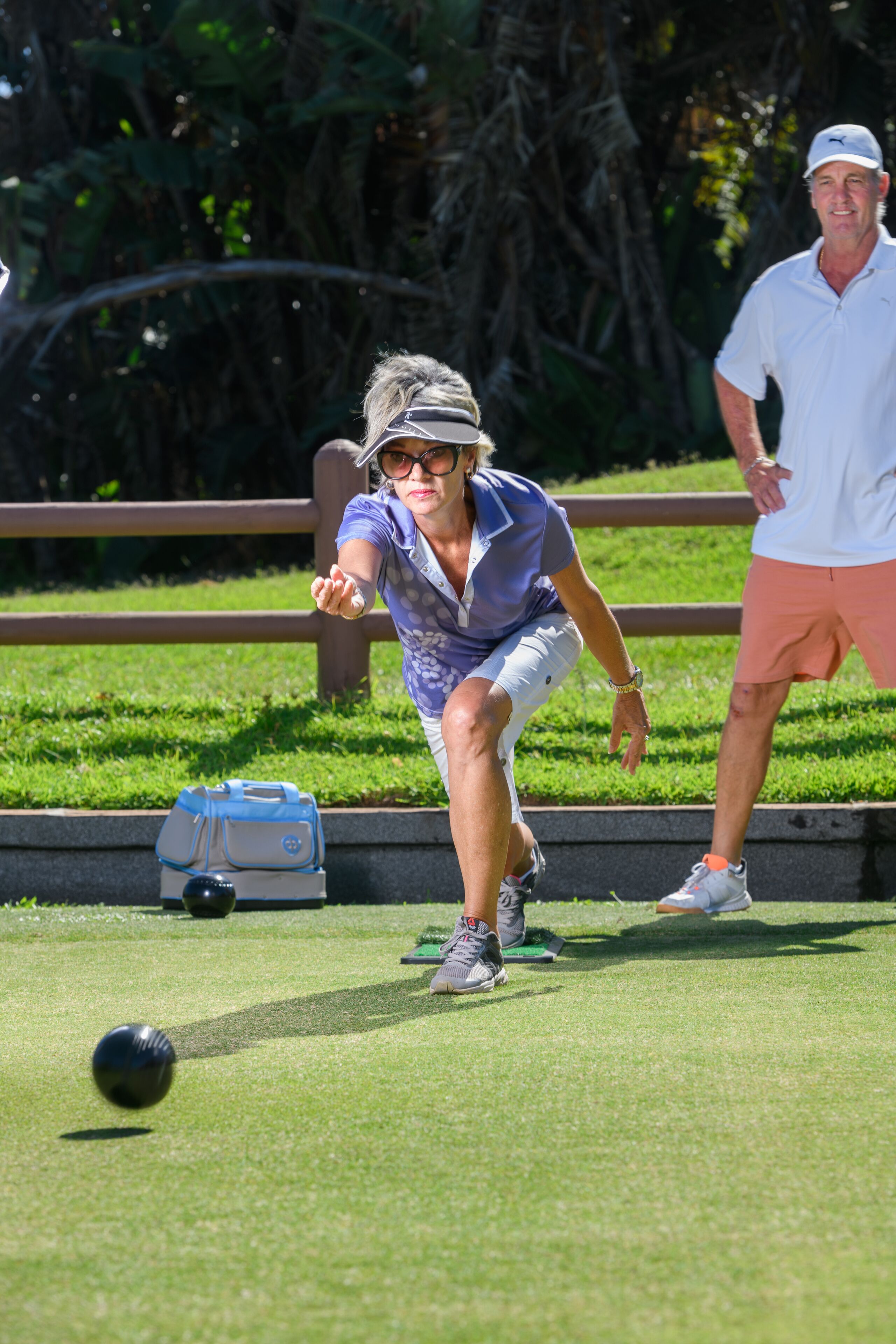 A person playing croquet on a grass field with a blue bag and a golf ball nearby.