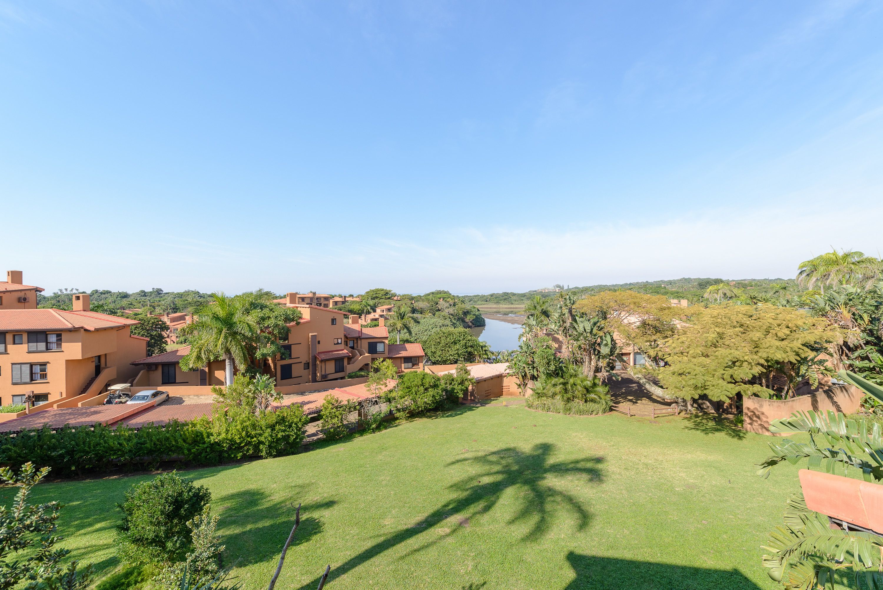 A residential area with multiple houses, a grassy lawn, and a body of water in the background.