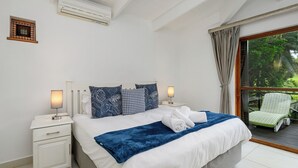 A bedroom with a bed, bedside lamps, a nightstand, a window with curtains, and a view of greenery outside. - San Lameer Villa Rentals  2707 (Southbroom)