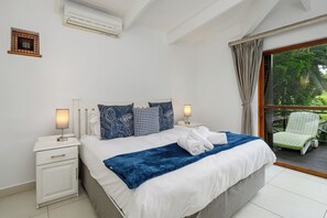 Una camera da letto con un letto, lampade da comodino, un comodino, una finestra con tende e vista sul verde.
