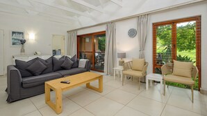 A modern living room with a sofa, coffee table, and chairs, large windows with curtains, and a clock on the wall. - San Lameer Villa Rentals  2707 (Southbroom)