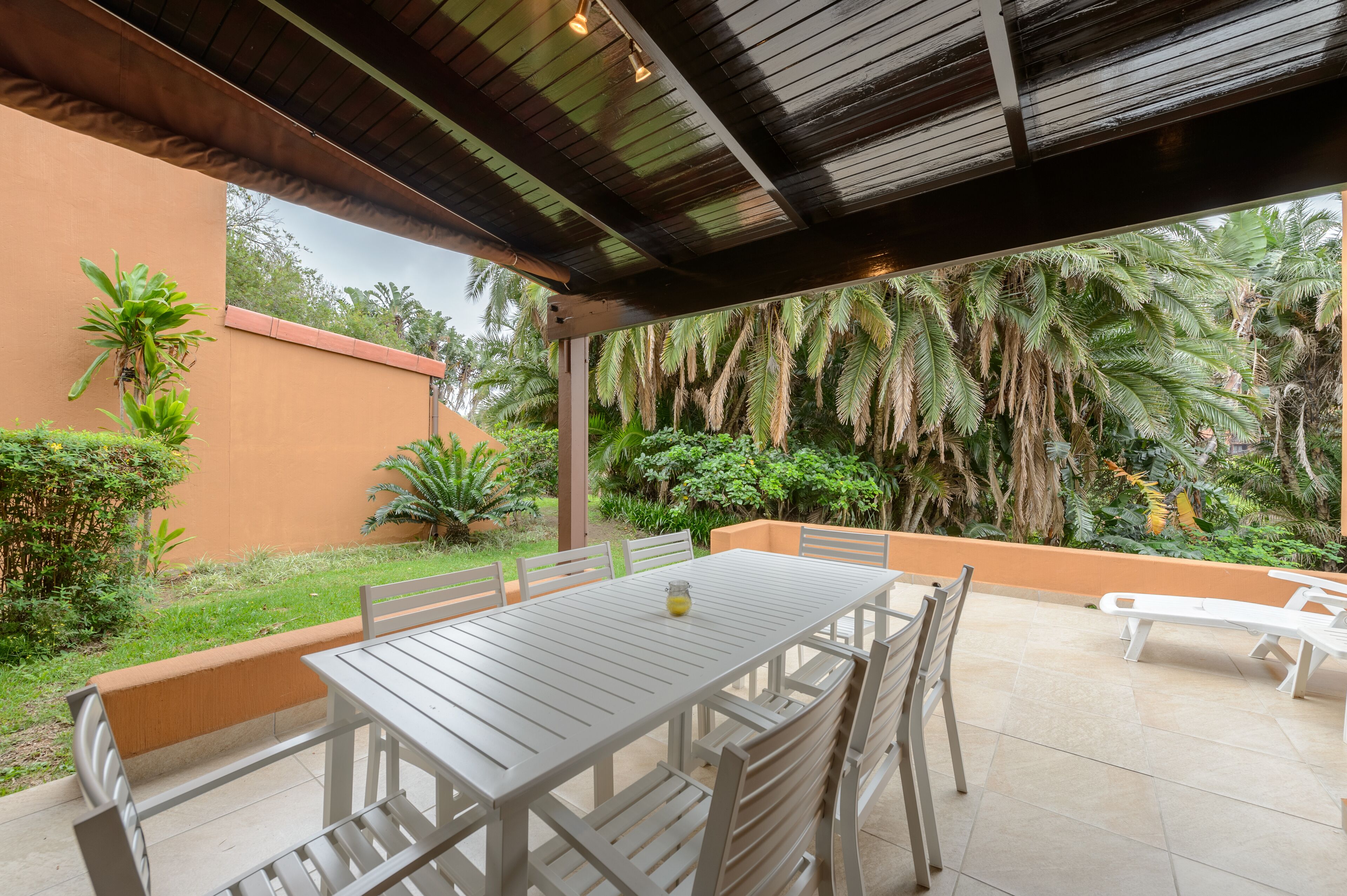 An outdoor patio with a table and chairs, surrounded by lush greenery and palm trees.