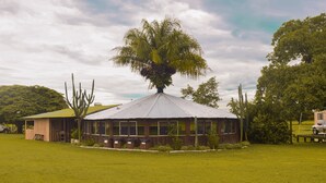 A circular building with a metal roof, surrounded by a grassy field, and a large tree in the center. - Pousada São João - Estrada Parque Pantanal (Corumba)