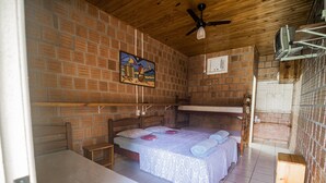 A room with a brick wall, a wooden ceiling, a bed with a white bedspread, a wooden nightstand, and a small table. - Pousada São João - Estrada Parque Pantanal (Corumba)