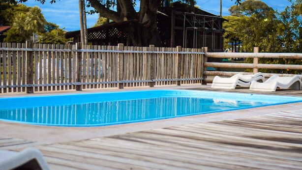 A wooden deck with a swimming pool, lounge chairs, and a covered area. - Pousada São João - Estrada Parque Pantanal (Corumba)