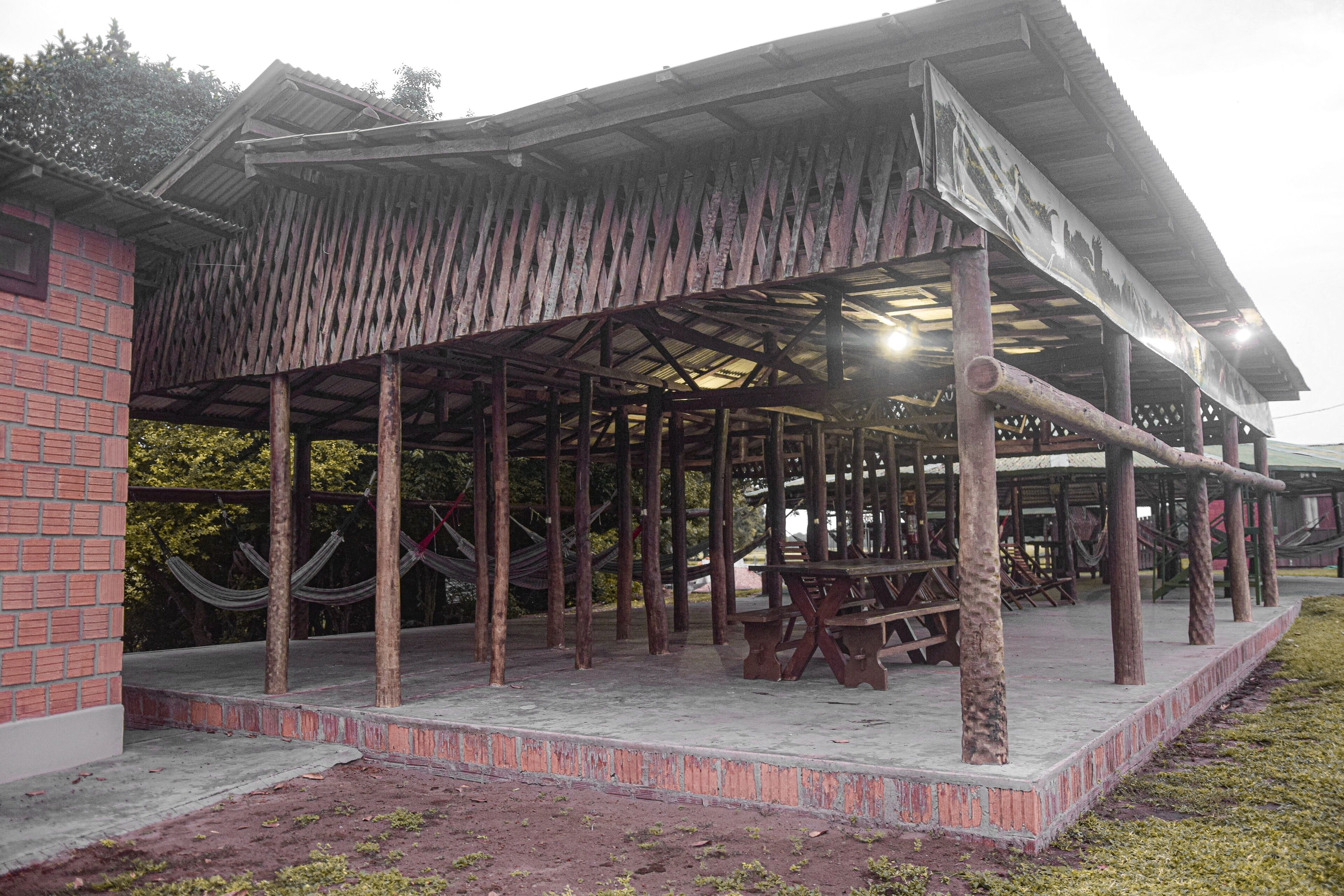 A wooden gazebo with a brick wall adjacent to it, featuring a concrete floor and several benches.