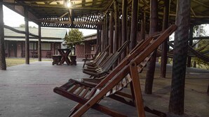 A covered outdoor area with wooden loungers and a table, surrounded by wooden pillars. - Pousada São João - Estrada Parque Pantanal (Corumba)