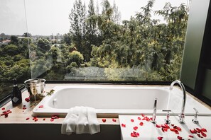 A bathroom with a bathtub, a window, and rose petals on the counter. - KAIDA Resort & Residences (Hang Dong)