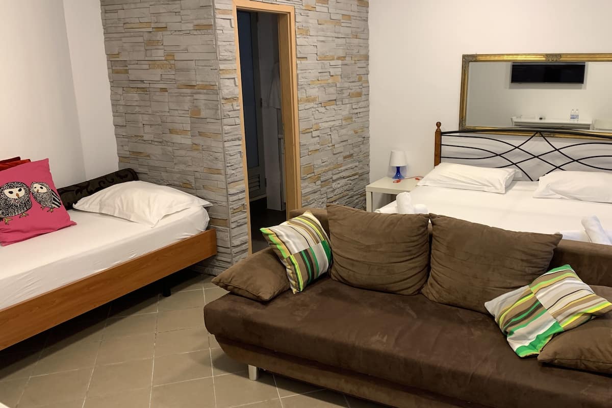 A bedroom with a bed, a brown sofa, a nightstand, a mirror, and a stone wall.