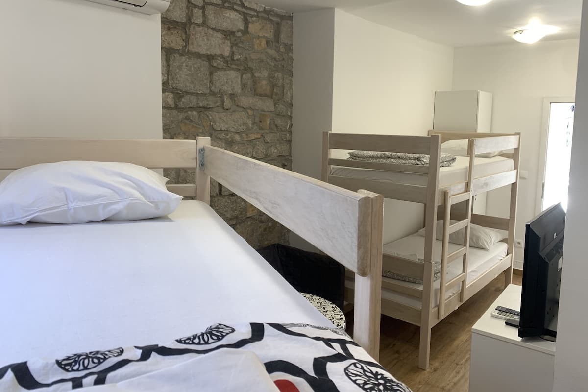 A room with a bunk bed, a single bed, a television, and a stone wall.