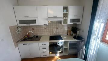 A compact kitchen with white cabinets, a sink, a stove, and a built-in oven.