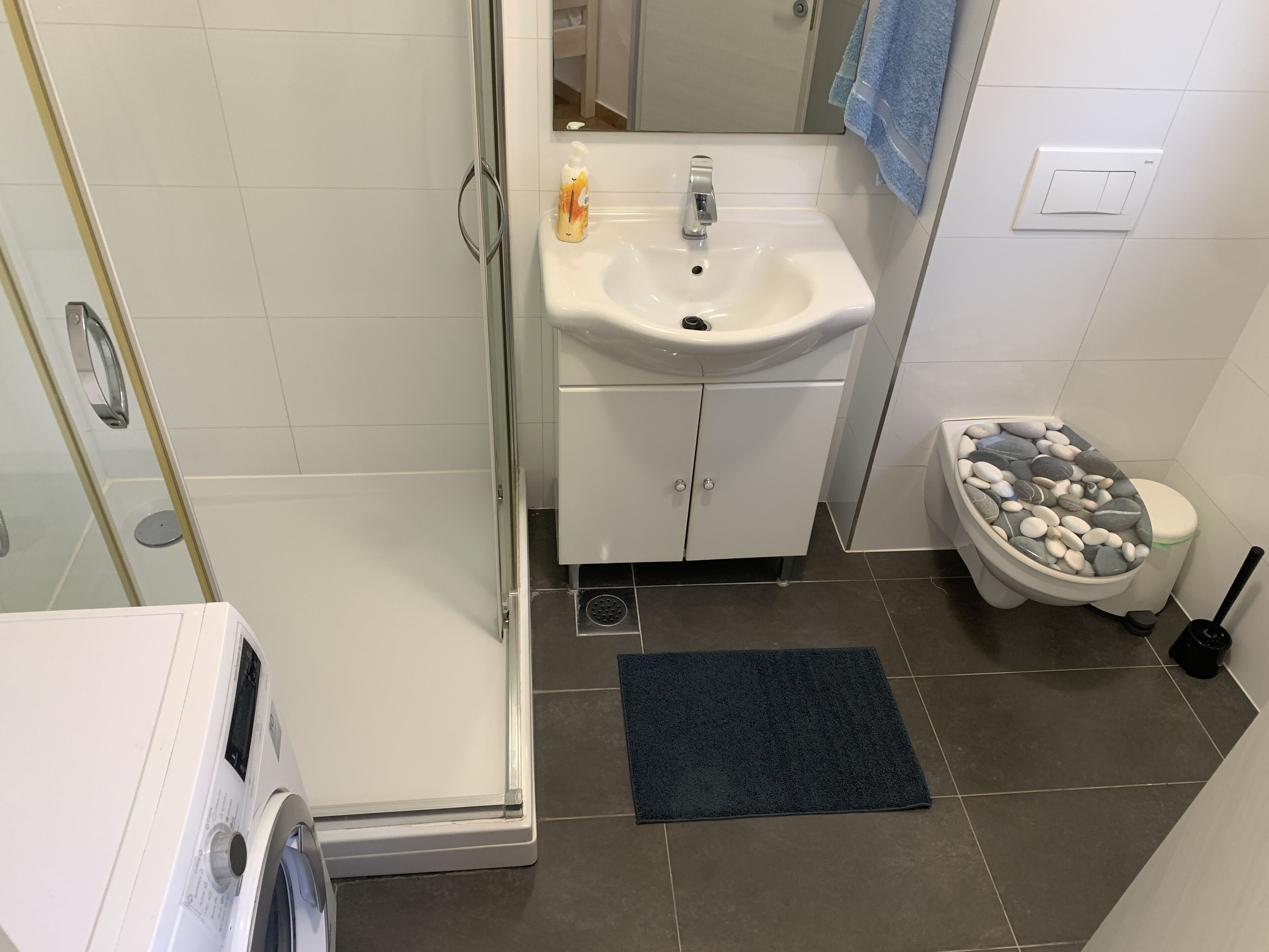 A bathroom with a shower, sink, toilet, and a washing machine.