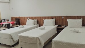 Una habitación de hotel con tres camas individuales, un cabecero de madera, una mesita con mantel rojo y una silla.