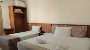 Habitación de hotel con dos camas, un armario de madera y una mesita de noche pequeña con un teléfono y una lámpara.