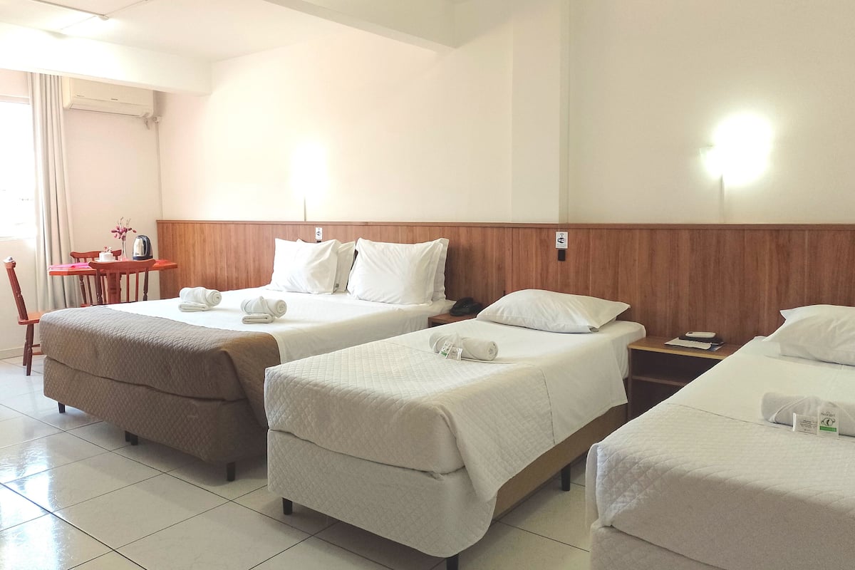 Una habitación de hotel con dos camas, una mesita con una silla y una ventana con cortinas.