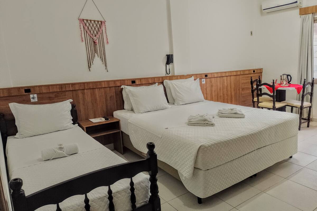 Habitación de hotel con dos camas, cabeceros de madera, ropa de cama blanca, una mesita de noche con lámpara, teléfono en la pared y una pequeña mesa con mantel rojo.