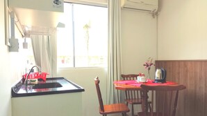 Habitación de hotel compacta con kitchenette, una mesa de comedor con sillas, ventana con cortinas y una cama.